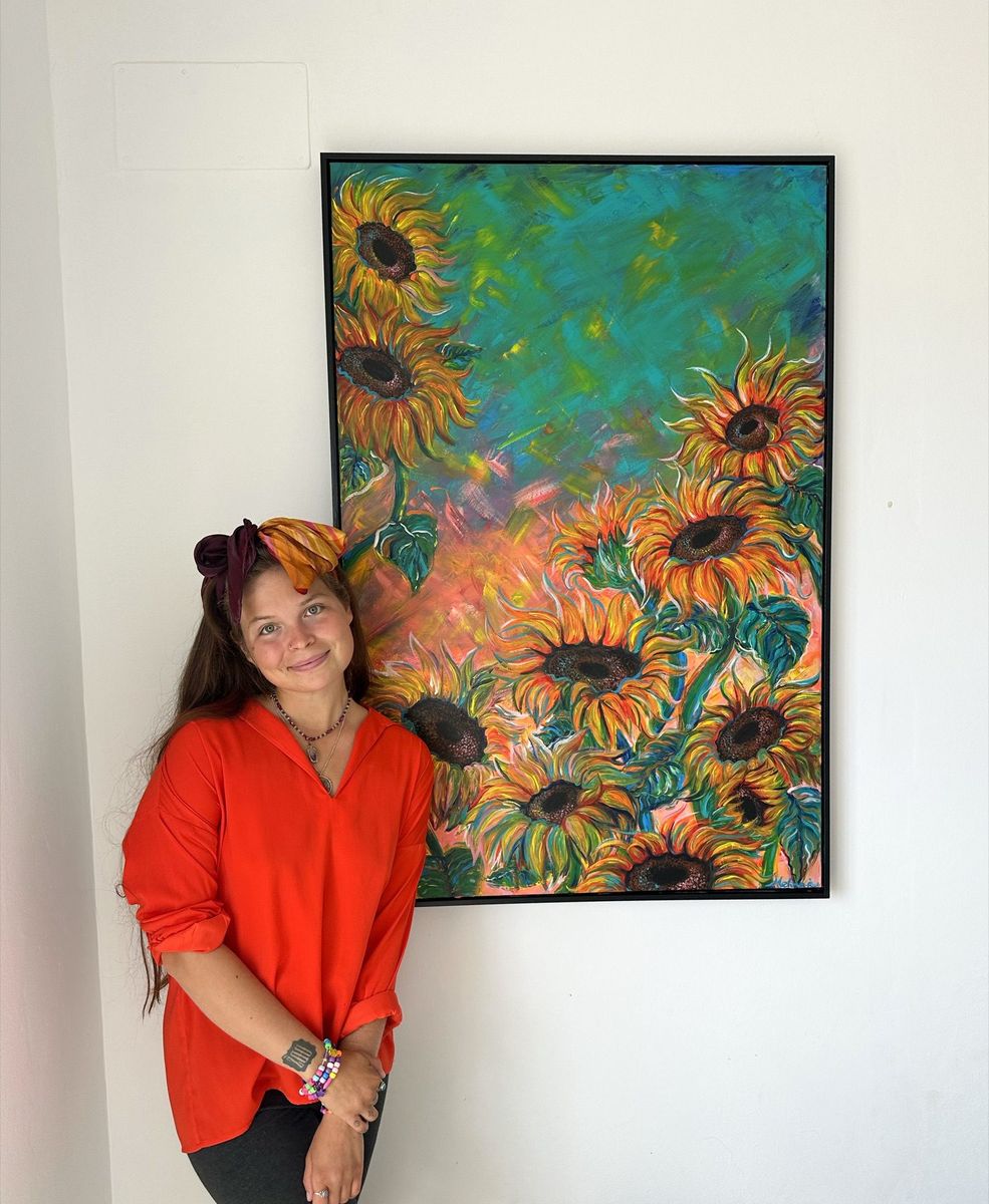 Melina standing beside her painting Sunflowers on a white wall